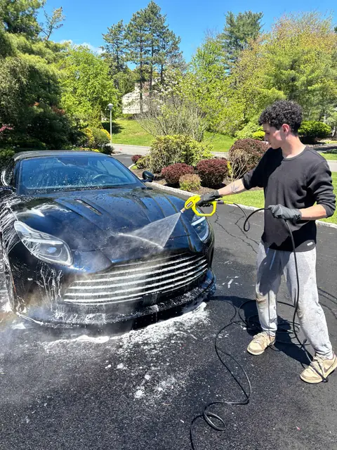 31 Auto Detailing technician foaming a black Aston Martin in a North Jersey driveway