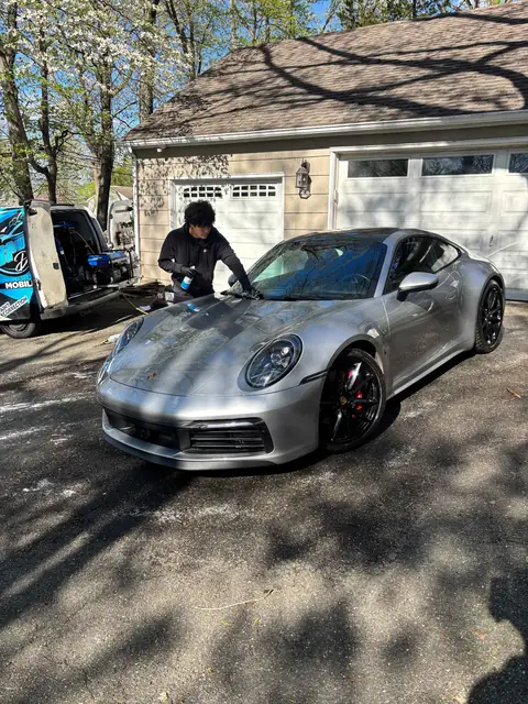 Technician finishing a silver Porsche 911 beside the detailing van
