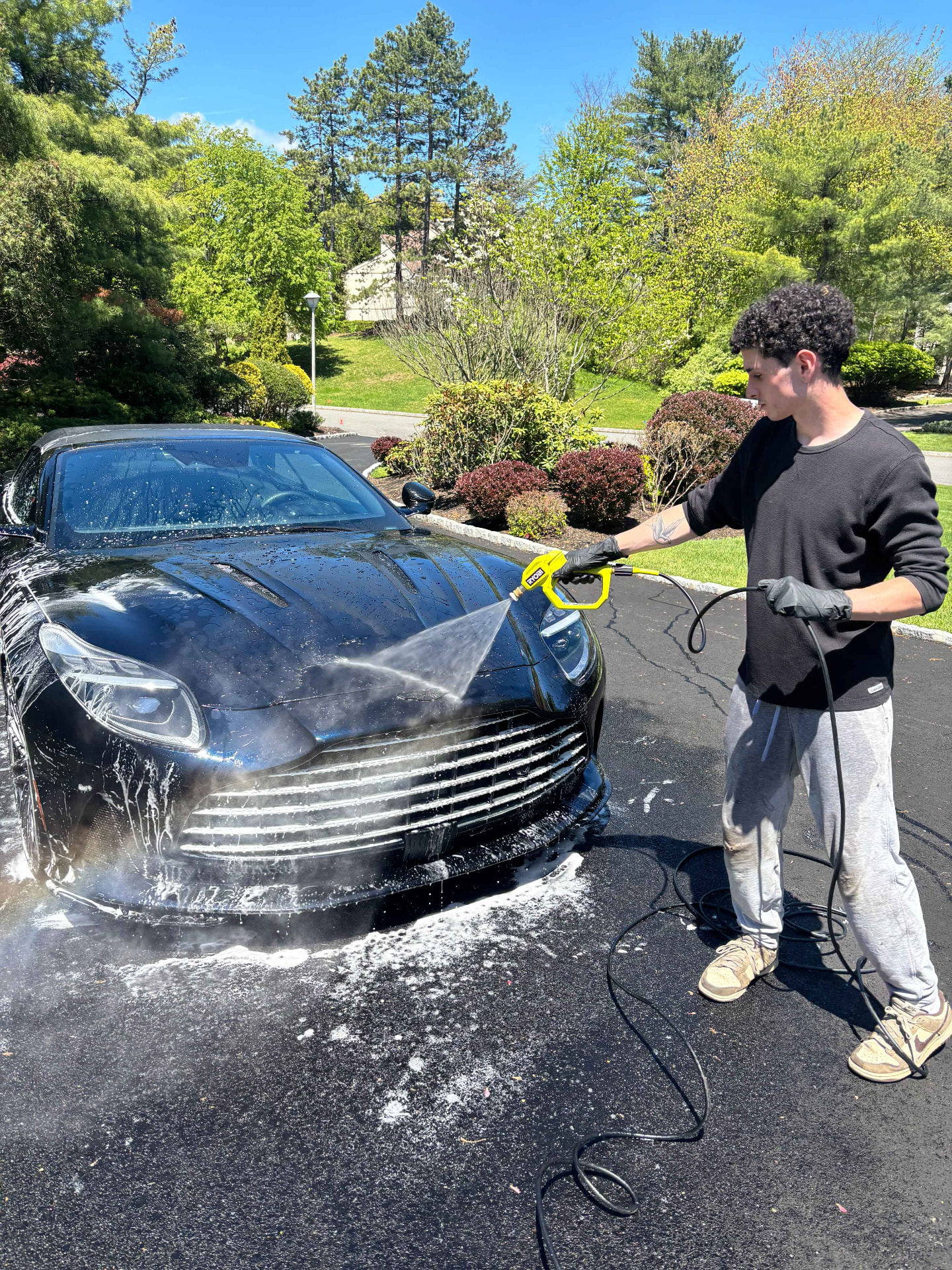 31 Auto Detailing technician foaming a black Aston Martin in a North Jersey driveway